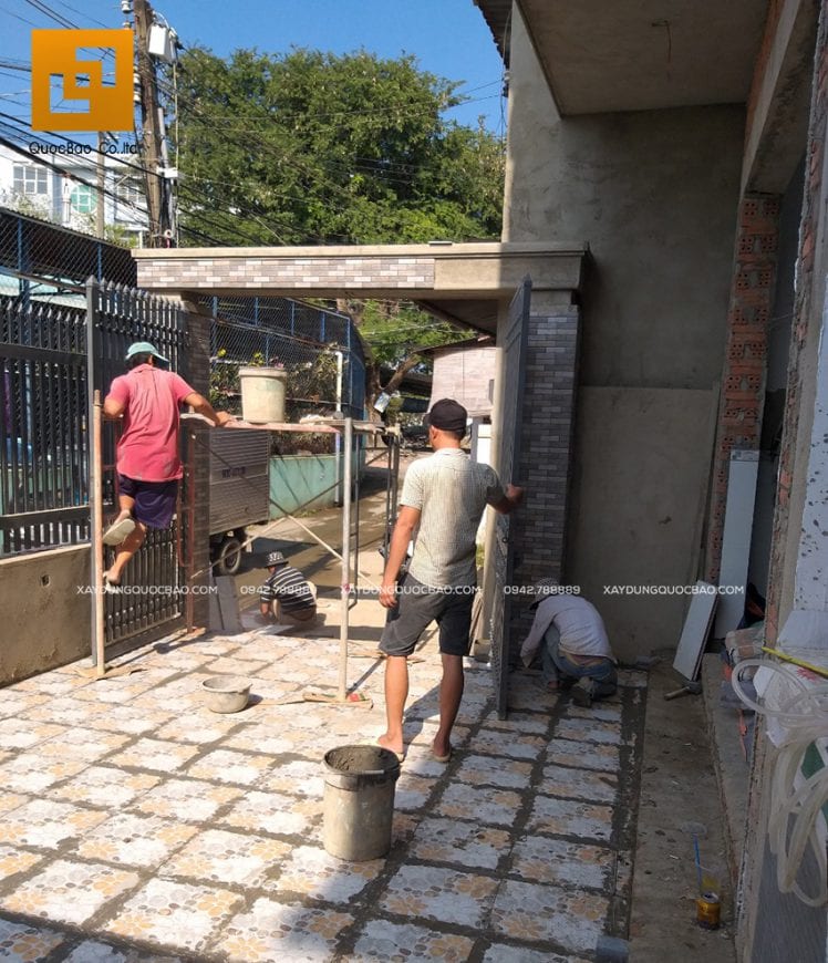 Công nhân thi công lót gạch nền sân và ốp đá trụ cổng nhà